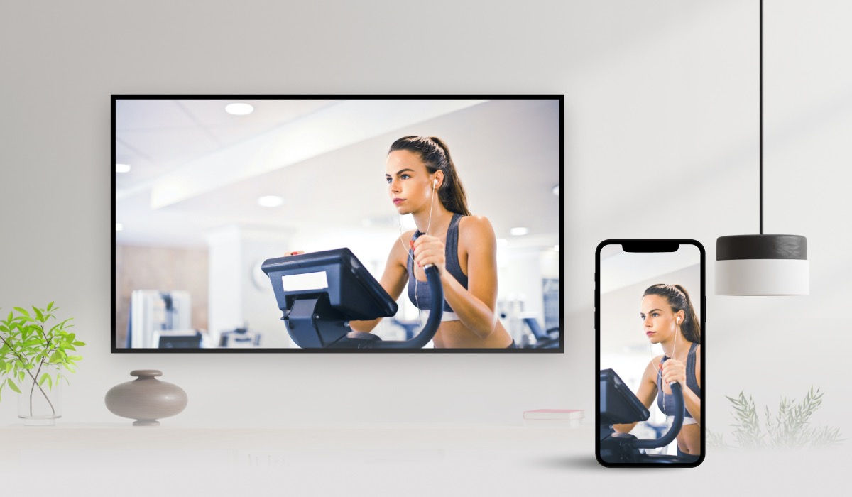 An iphone casting an image of a woman doing a stationary bike workout to a wall mounted LG TV