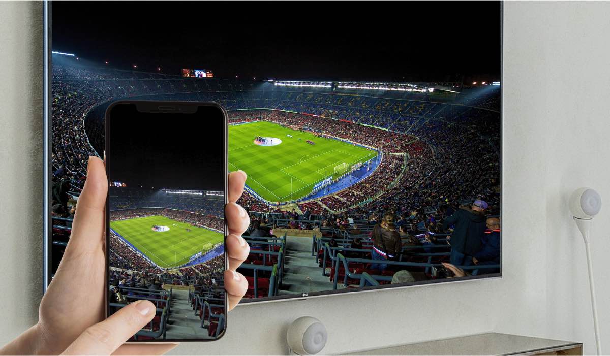 A hand holding an iPhone that is mirroring an image of a stadium to an LG TV