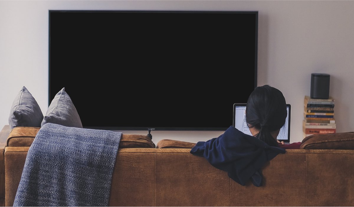 A person sitting on a couch with a laptop. A Smart tV in front of the person with black screen