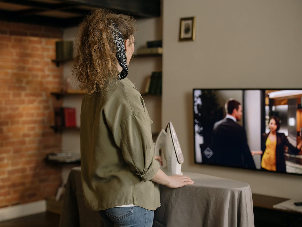 Woman watching a TV series on a Smart TV while ironing